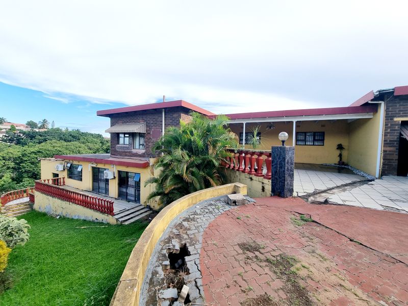 Rear view of the property featuring a multi-level layout, paved patio areas, and a garden, showing signs of wear on the exterior finishes and paving.