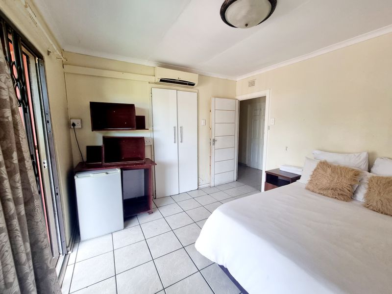 A functional bedroom featuring tiled flooring, a built-in wardrobe, a split-system air conditioner, and direct access to an outdoor area via a sliding glass door.