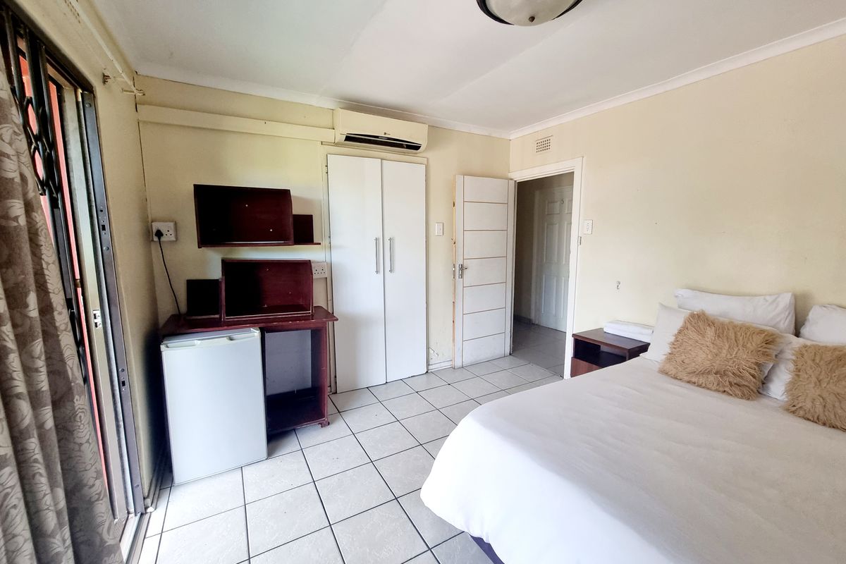 A functional bedroom featuring tiled flooring, a built-in wardrobe, a split-system air conditioner, and direct access to an outdoor area via a sliding glass door.