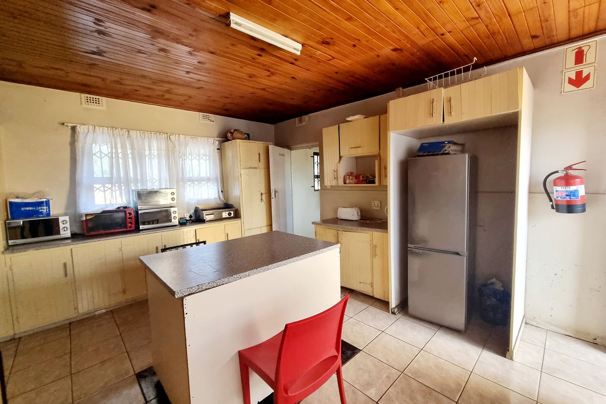 A functional kitchen featuring timber ceiling paneling, tiled flooring, and ample laminate cabinetry with a central island workspace.