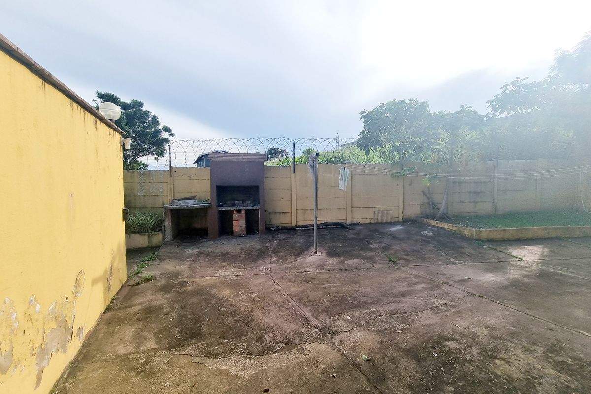Rear outdoor area featuring a built-in braai, concrete paving, and a perimeter wall with security fencing.