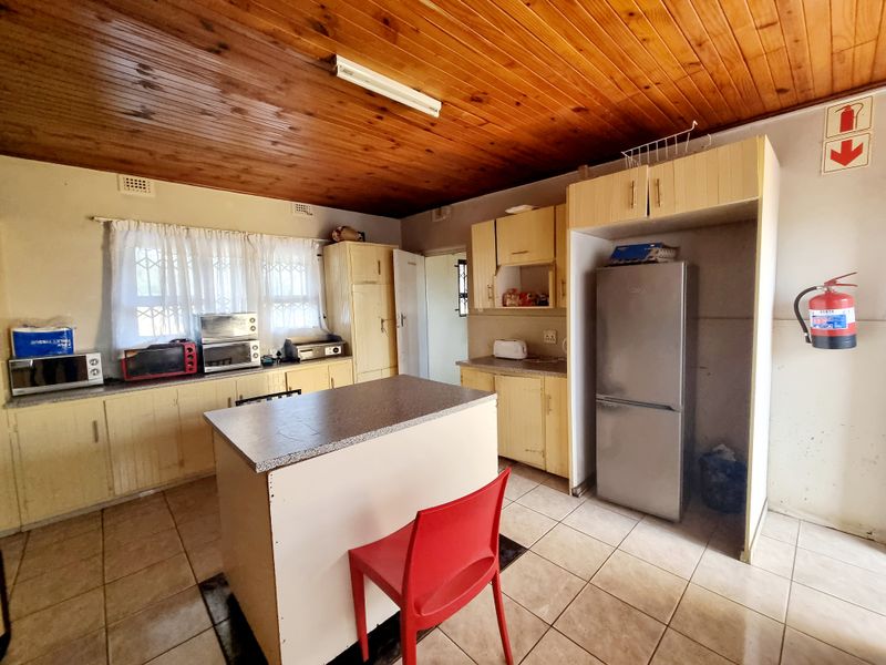 A functional kitchen featuring timber ceiling paneling, tiled flooring, and ample laminate cabinetry with a central island workspace.
