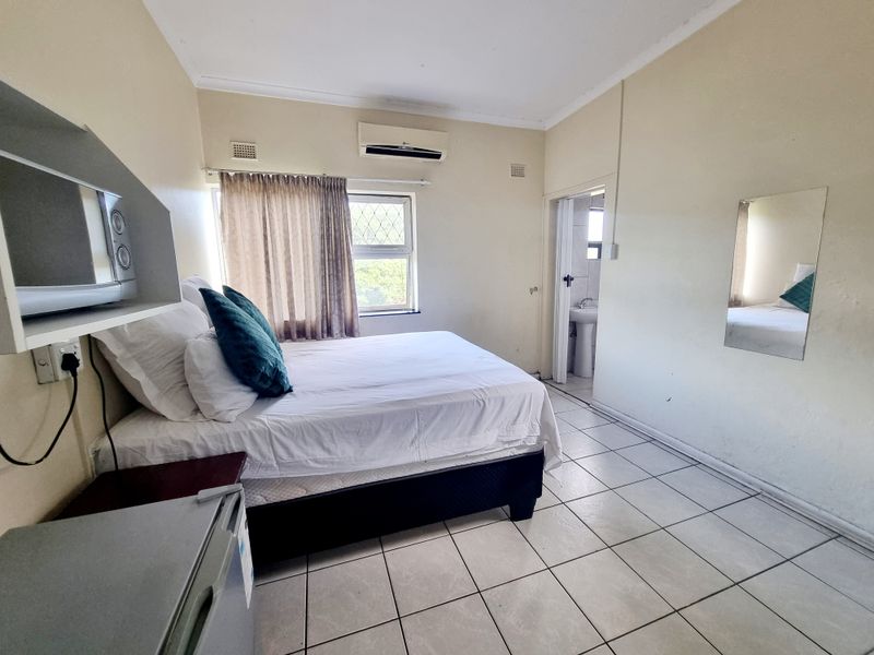 A functional bedroom featuring tiled flooring, an integrated air conditioning unit, and direct access to an en-suite bathroom.