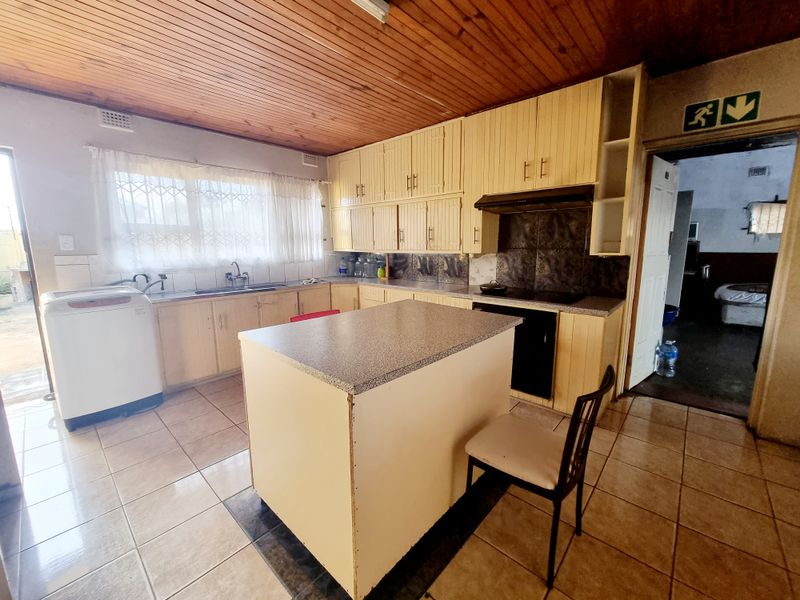 A dated kitchen featuring timber ceilings, built-in cabinetry, a central island, and tiled flooring, offering potential for a modern renovation.