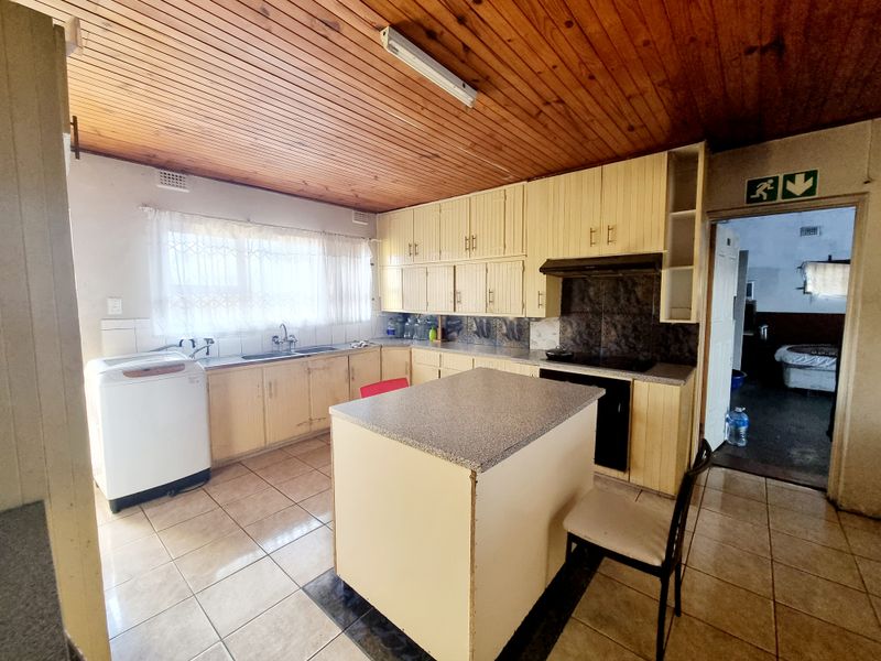 A dated kitchen featuring timber ceilings, tiled flooring, built-in cabinetry, and a central island, offering significant potential for a modern renovation.