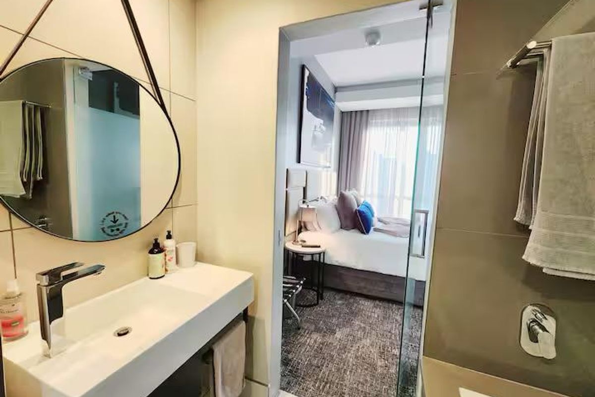 Modern bathroom featuring a sleek wall-mounted vanity and basin, with a glass door providing a view into the adjacent bedroom.