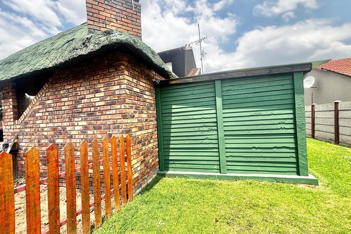 A view of the rear garden area featuring a brick structure with a thatch roof and an adjacent green timber storage or utility enclosure.