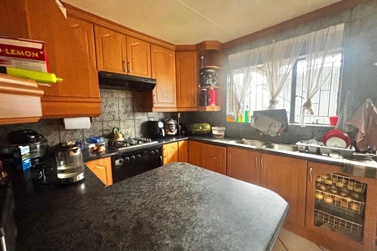 A functional kitchen featuring wooden cabinetry, dark laminate countertops, a built-in gas hob, and a double basin sink with security bars on the window.
