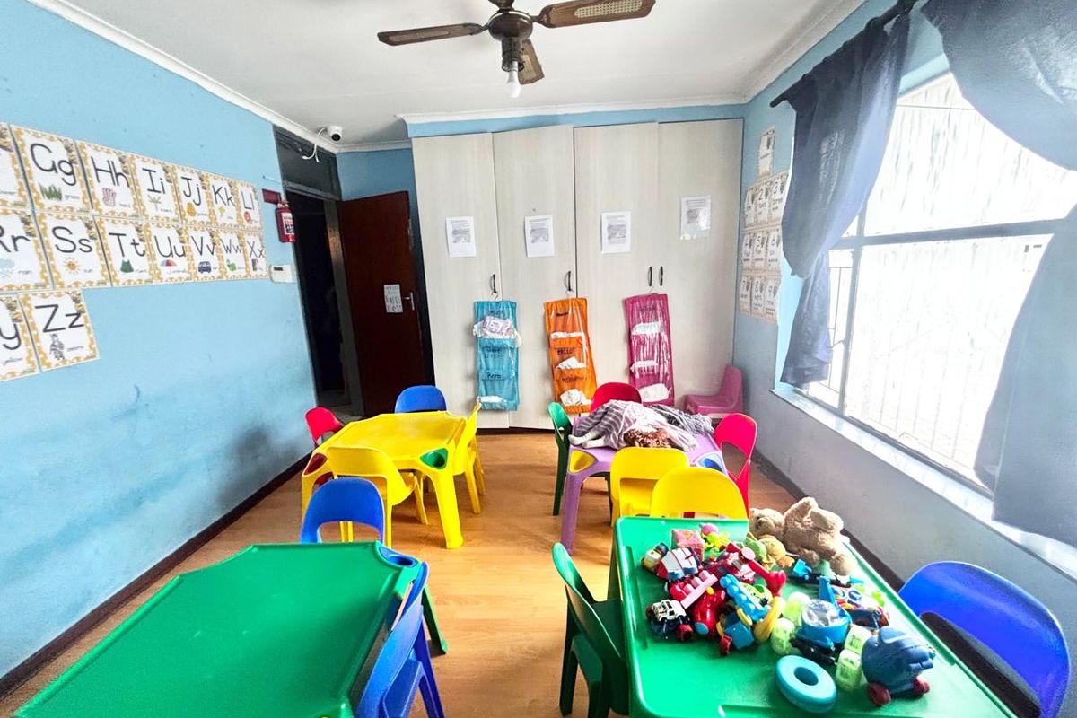 A functional room currently utilized as a classroom, featuring built-in storage cupboards, a ceiling fan, and large windows providing natural light.