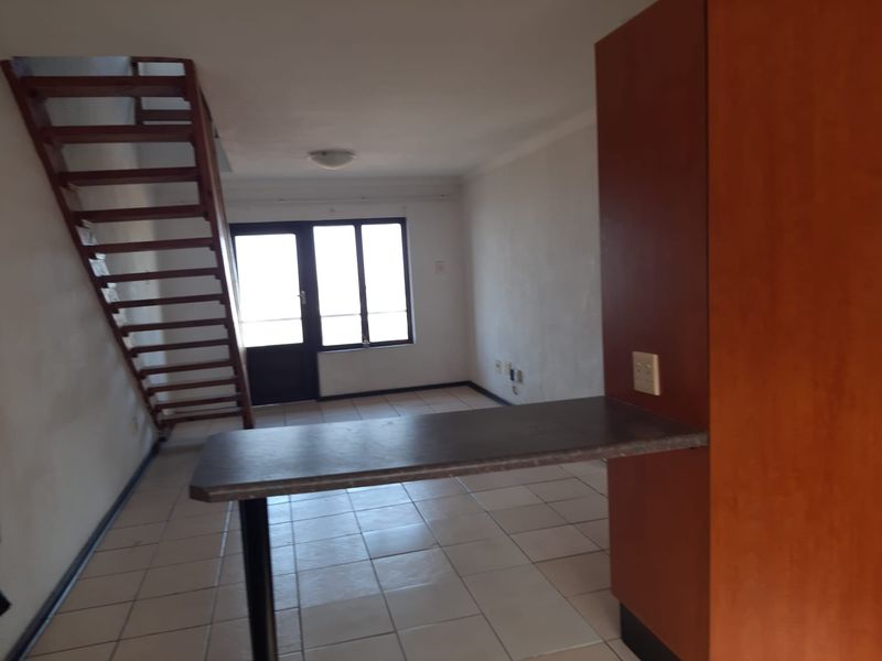 An open-plan living area featuring tiled flooring, a breakfast bar, and an open staircase leading to the upper level.