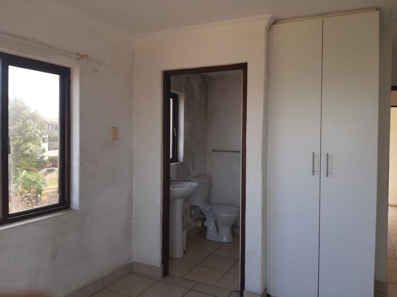 A bedroom featuring tiled flooring, a built-in wardrobe, and an en-suite bathroom with a pedestal basin and toilet.