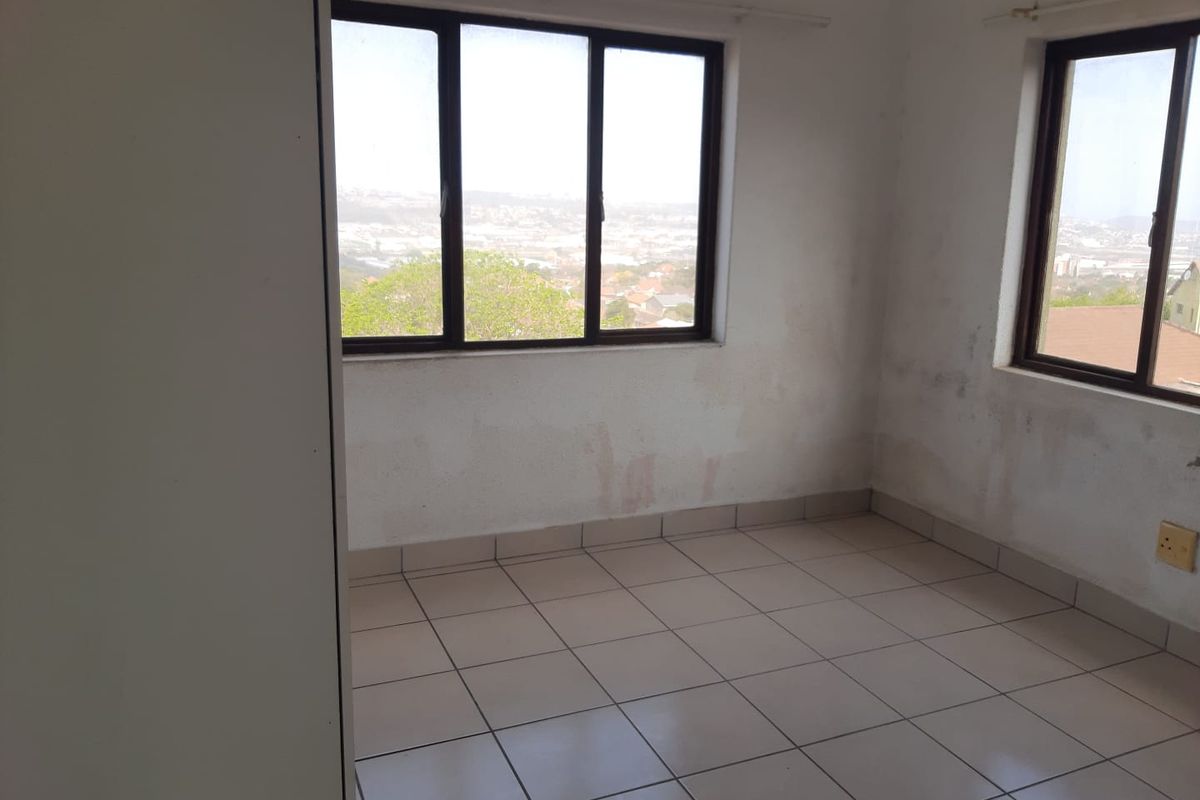 An empty bedroom featuring tiled flooring and large windows with views, requiring cosmetic attention to address wall staining and paint condition.