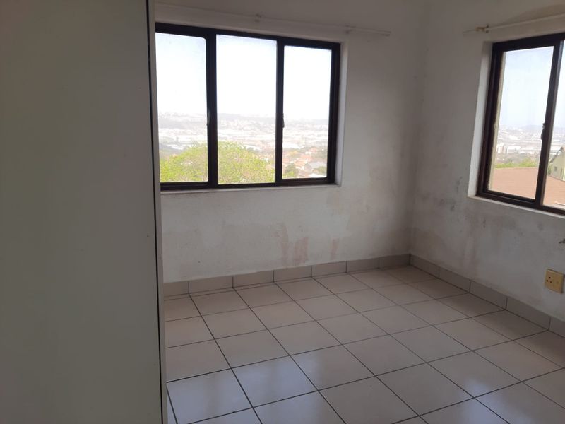 An empty bedroom featuring tiled flooring and large windows with views, requiring cosmetic attention to address wall staining and paint condition.