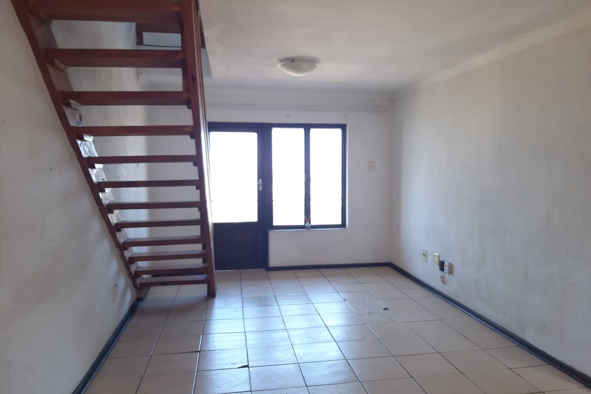 An empty living area featuring tiled flooring, a wooden staircase leading to an upper level, and access to an outdoor space via a sliding door.