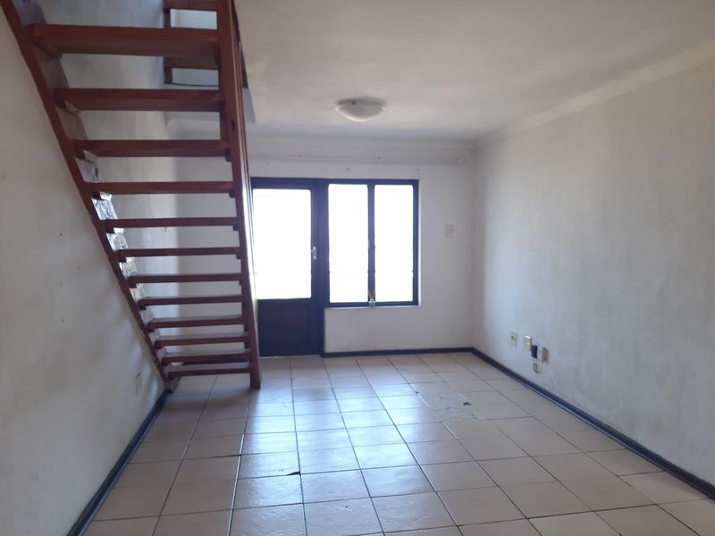 An empty living area featuring tiled flooring, a wooden staircase leading to an upper level, and access to an outdoor space via a sliding door.