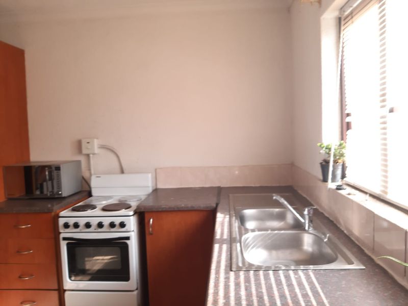 A compact kitchen featuring a freestanding stove, double bowl stainless steel sink, laminate countertops, and built-in cabinetry with a tiled splashback.
