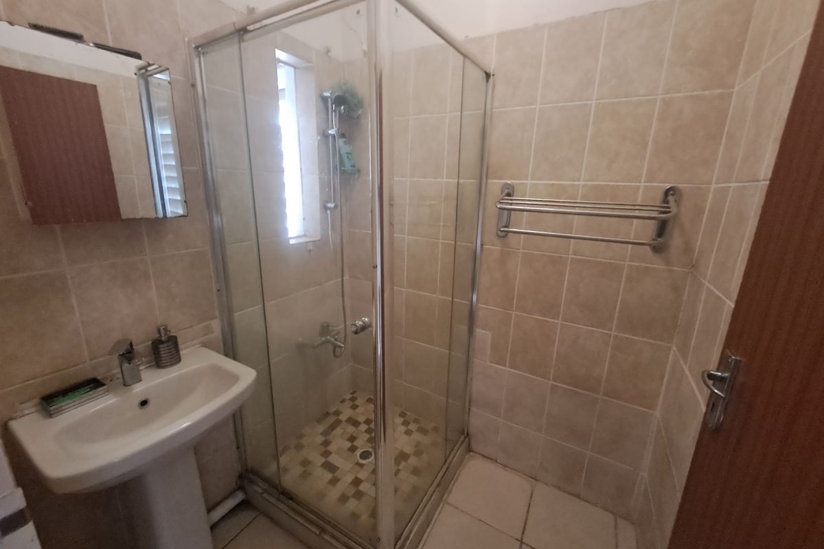 A compact bathroom featuring a pedestal basin, a glass shower enclosure, and neutral wall and floor tiling.