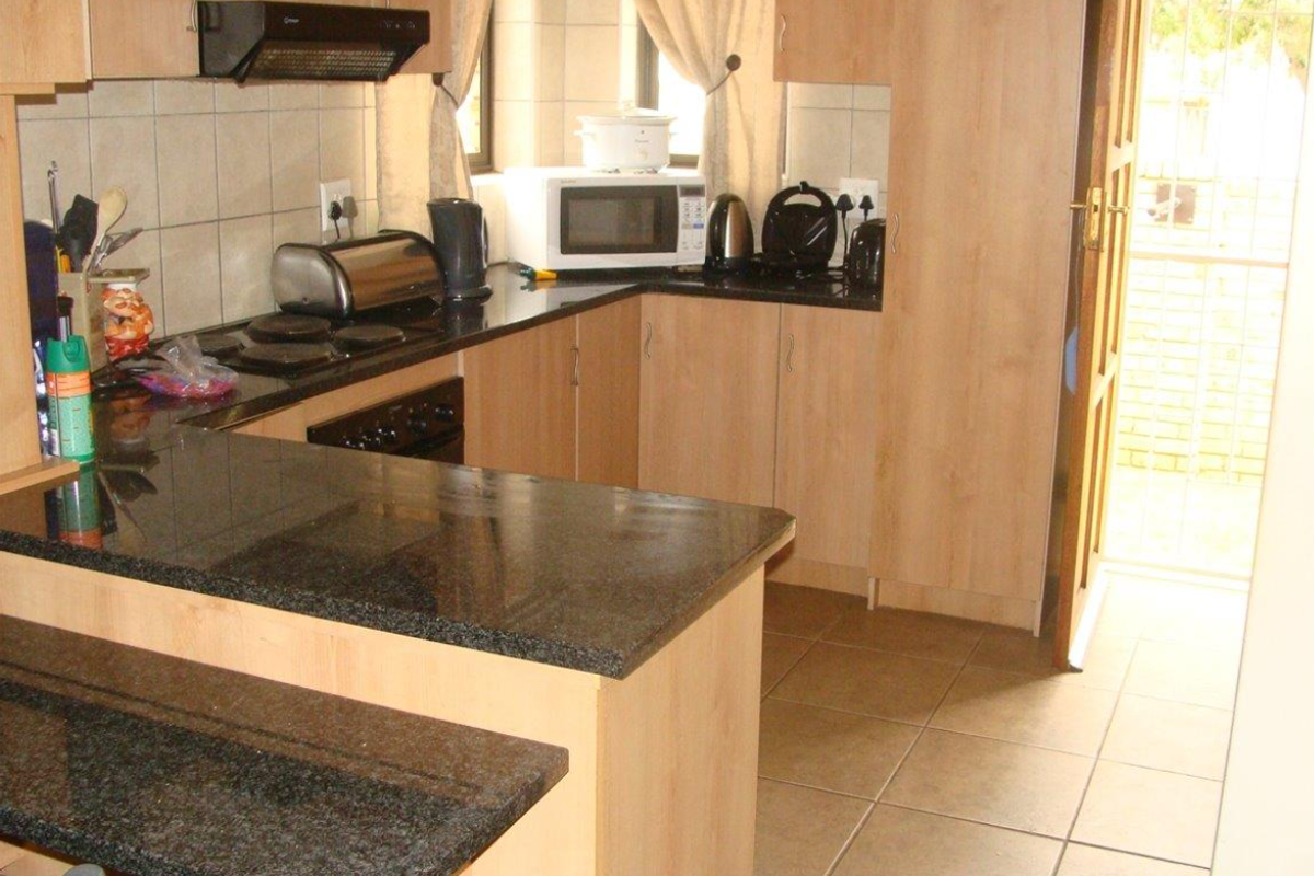Functional kitchen featuring granite countertops, laminate cabinetry, built-in oven, electric hob, and tiled flooring with direct access to the exterior.