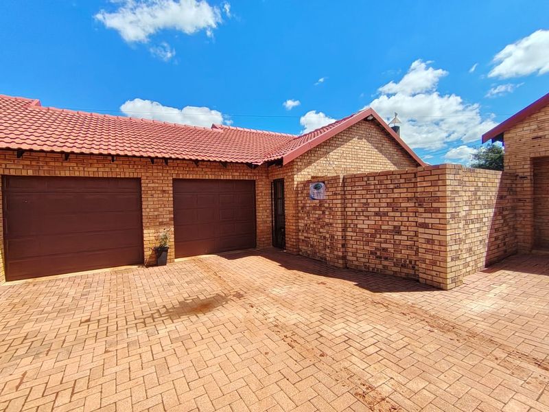A well-maintained face brick house exterior featuring a double garage, tiled roof, and a paved driveway.