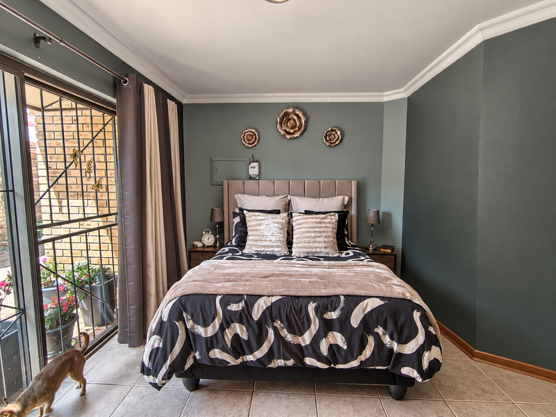 A well-maintained bedroom featuring tiled flooring, crown molding, and a large sliding glass door with an integrated security gate providing access to the outdoors.