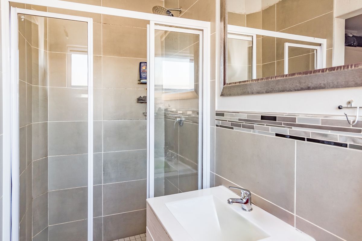 A modern bathroom featuring a glass-enclosed shower, a vanity with a basin, and neutral wall tiling with a decorative mosaic accent strip.