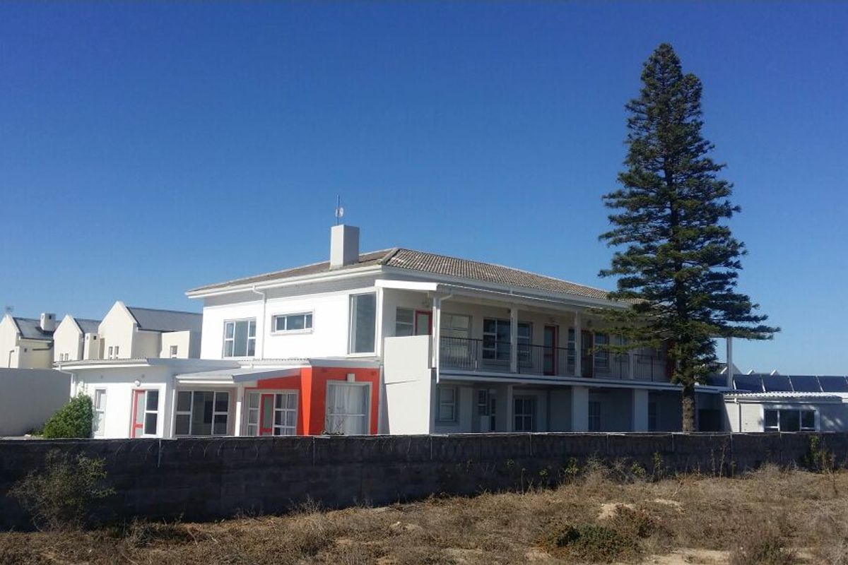 Rear view of a multi-story guest house featuring a balcony, tiled roof, and solar panels, enclosed by a perimeter wall with security wire.