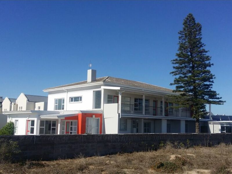 Rear view of a multi-story guest house featuring a balcony, tiled roof, and solar panels, enclosed by a perimeter wall with security wire.