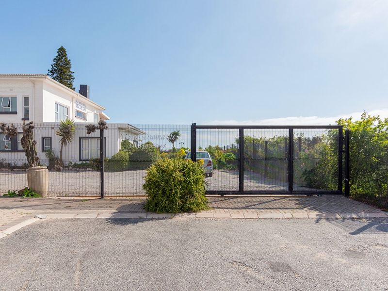 Street view of the guest house entrance featuring a secure gated access point, paved driveway, and gravel parking area.