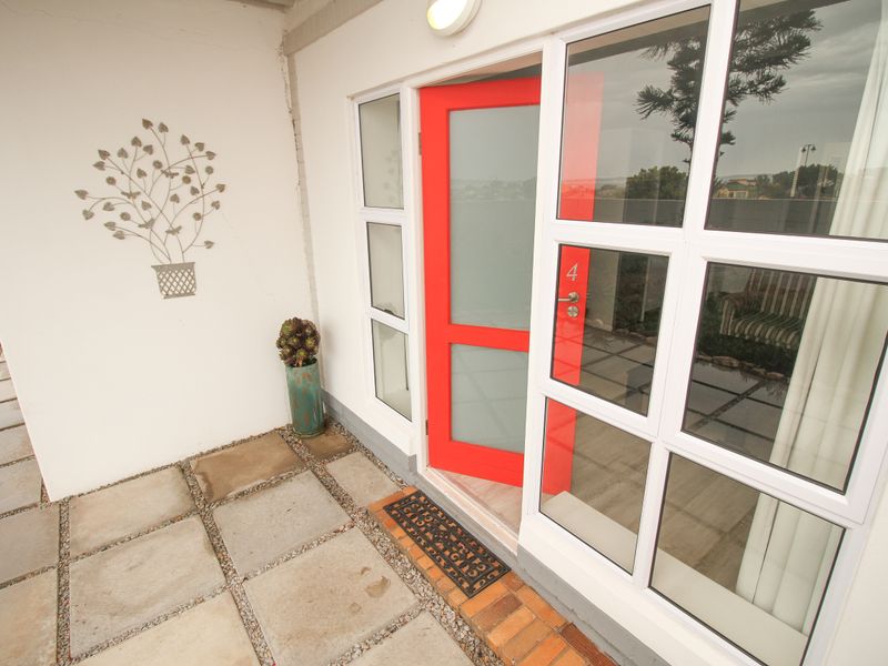 A clean, paved patio area featuring a bright red entrance door with glass panels and modern aluminium window frames.