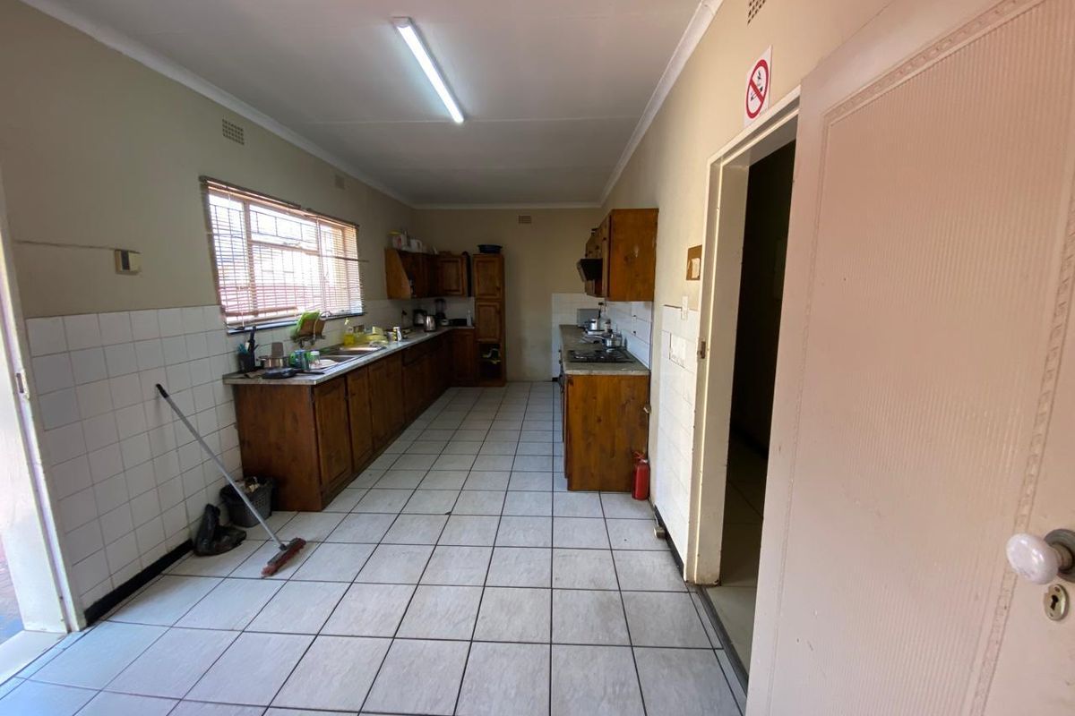 A functional, dated kitchen featuring wooden cabinetry, tiled flooring, and a built-in hob, offering a blank canvas for modern renovation.