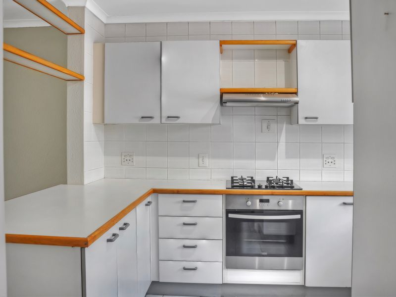A clean, functional kitchen featuring white cabinetry, a gas hob, built-in oven, extractor fan, and tiled backsplash with wooden countertop accents.