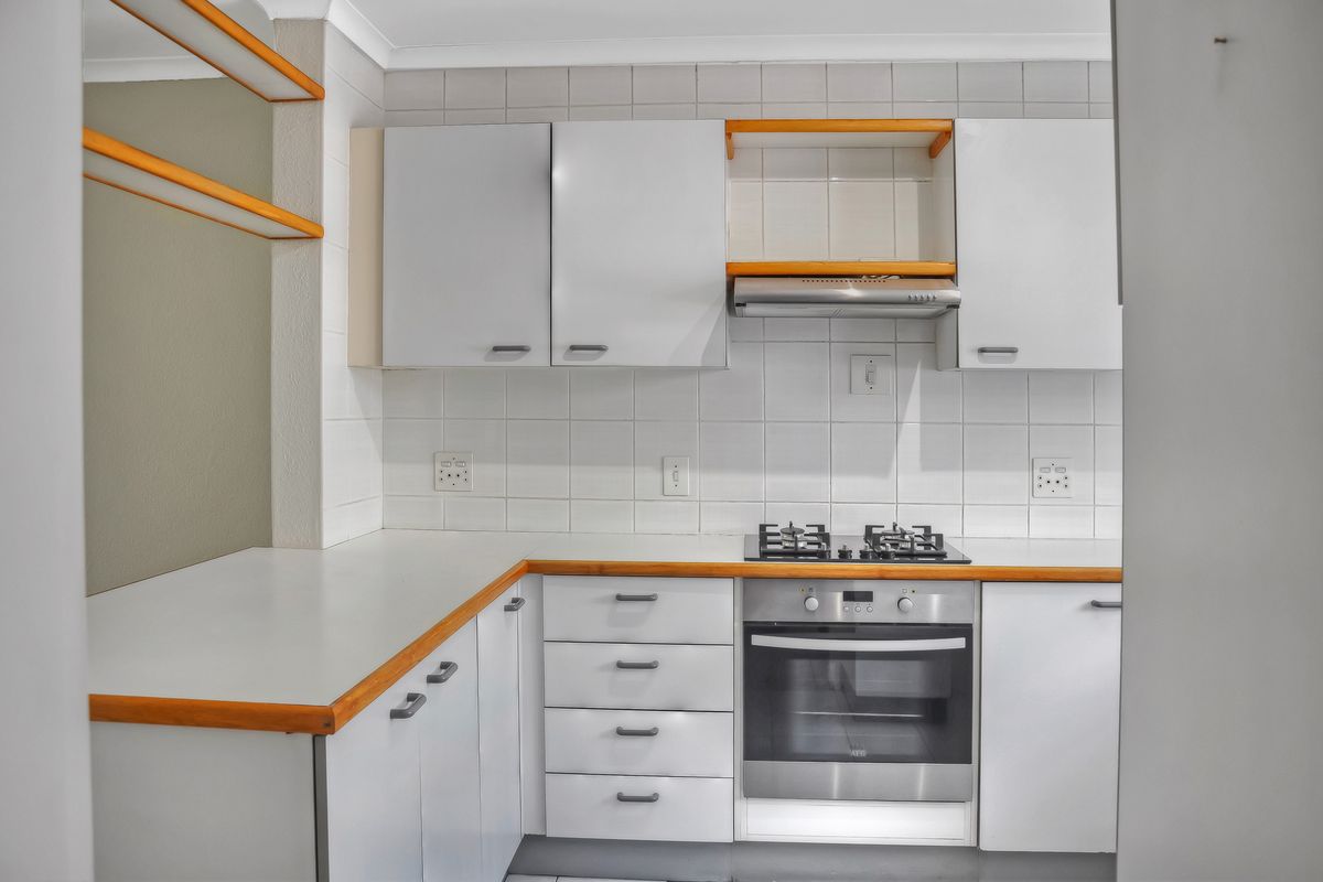 A clean, functional kitchen featuring white cabinetry, a gas hob, built-in oven, extractor fan, and tiled backsplash with wooden countertop accents.