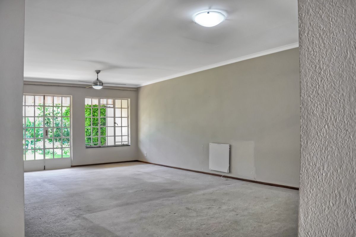 Spacious, empty living room featuring a ceiling fan, wall-mounted heater, and large windows with access to the garden area.