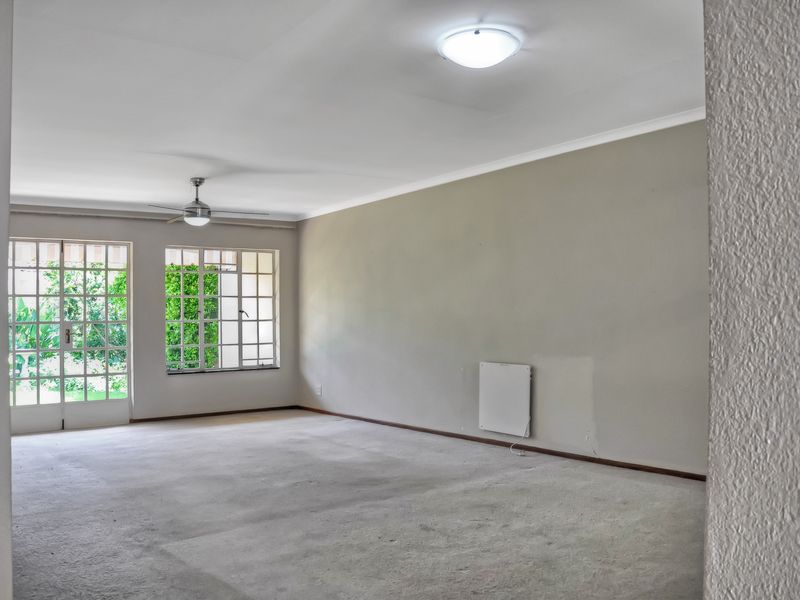 Spacious, empty living room featuring a ceiling fan, wall-mounted heater, and large windows with access to the garden area.