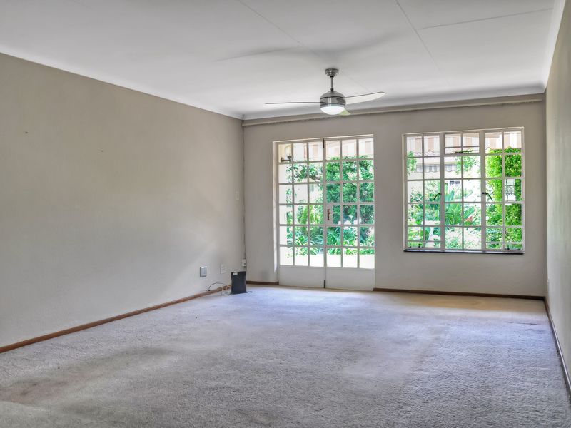 Spacious, empty living room featuring a ceiling fan, wall-mounted heater, and large grid windows with garden views.