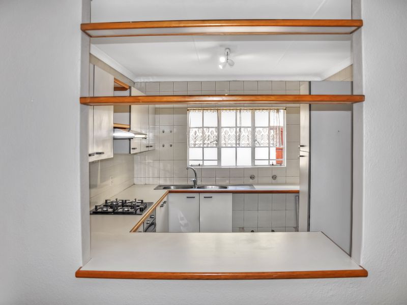 A functional kitchen featuring a gas hob, built-in oven, extractor fan, and a convenient pass-through window connecting to the adjacent living area.