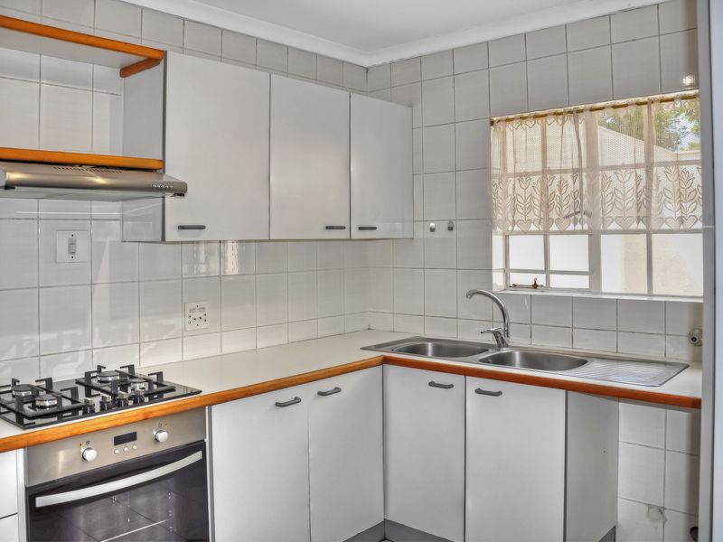 A functional kitchen featuring white cabinetry, a gas hob, built-in oven, and a double stainless steel sink with tiled splashbacks.