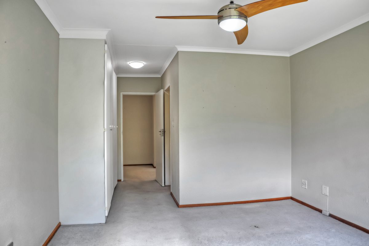 An empty bedroom featuring built-in cupboards, a ceiling fan, and neutral wall tones, offering a blank canvas for personalization.