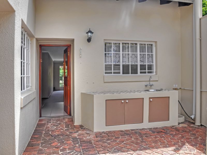 A covered outdoor patio area featuring brick paving, a built-in sink with cabinetry, and direct access to the interior of the townhouse.