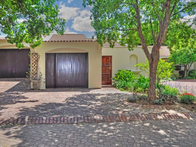 Front elevation of a townhouse featuring a double garage, paved driveway, and established garden with mature trees.