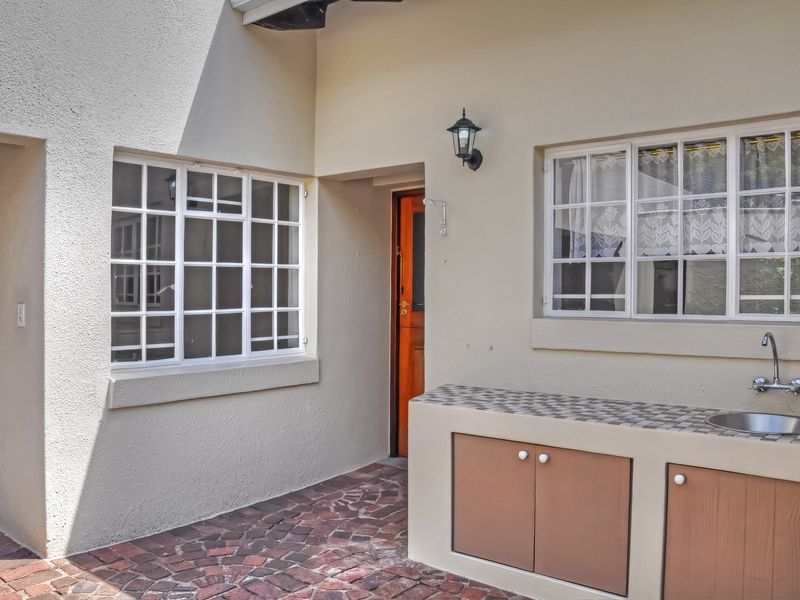 A paved rear courtyard area featuring a built-in outdoor sink, cabinetry, and access to the main dwelling through a timber door.