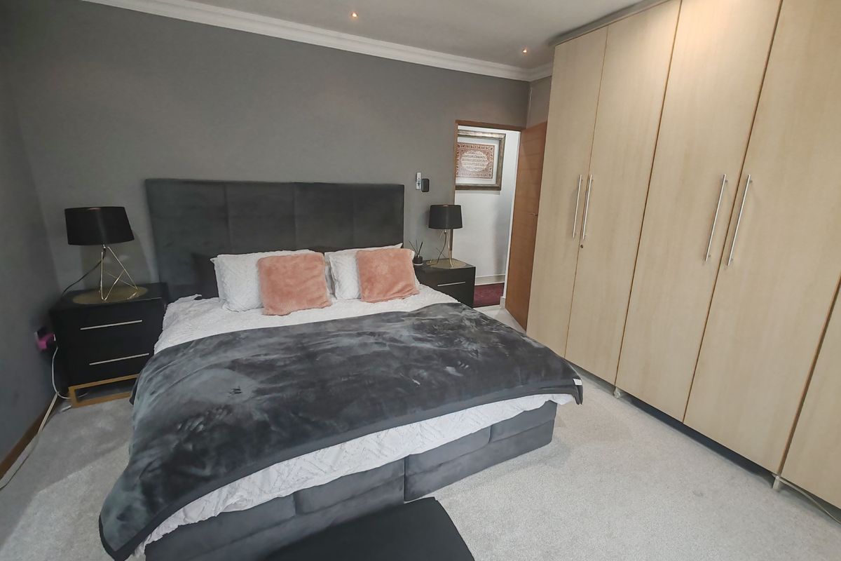 A well-maintained bedroom featuring neutral carpeting, grey accent wall, and extensive light wood built-in cabinetry with modern hardware.