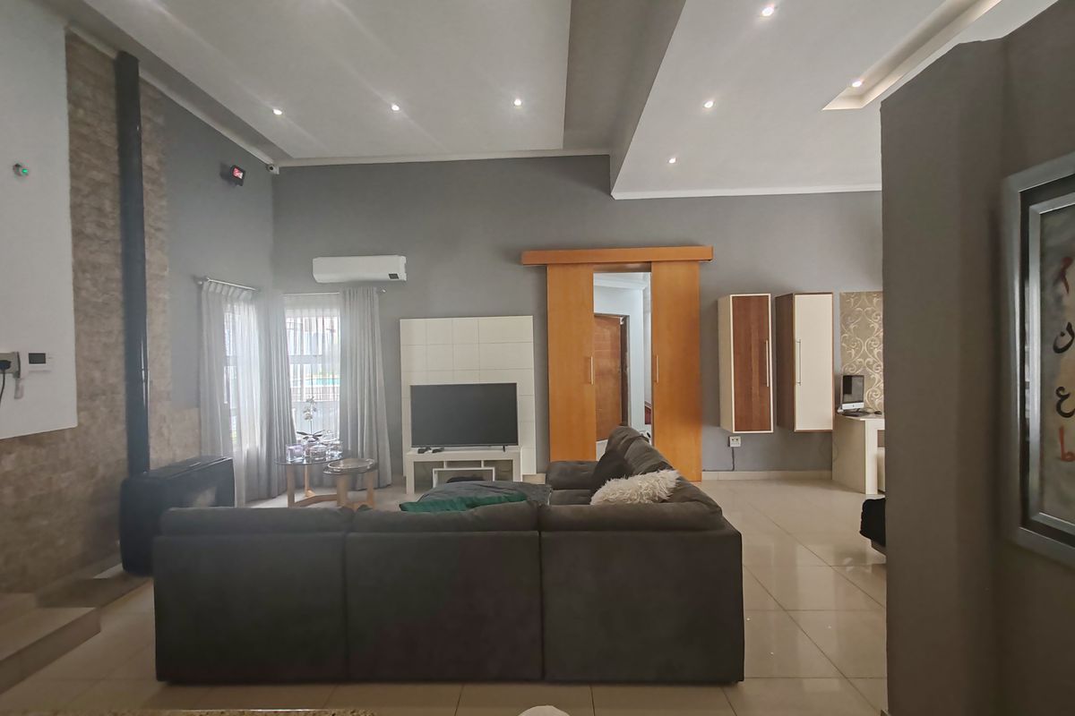 Spacious living room featuring a stone-clad feature wall, modern recessed ceiling lighting, tiled flooring, and a split-system air conditioner for climate control.