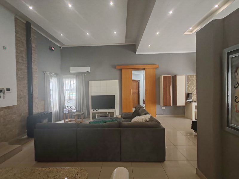 Spacious living room featuring a stone-clad feature wall, modern recessed ceiling lighting, tiled flooring, and a split-system air conditioner for climate control.