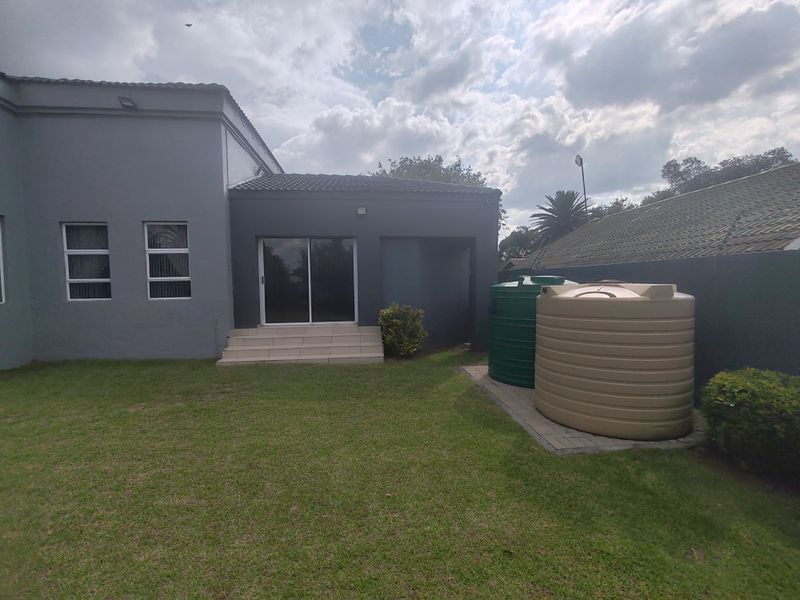 Rear view of the property featuring a lawn, sliding door access, and two large water storage tanks on a paved base.