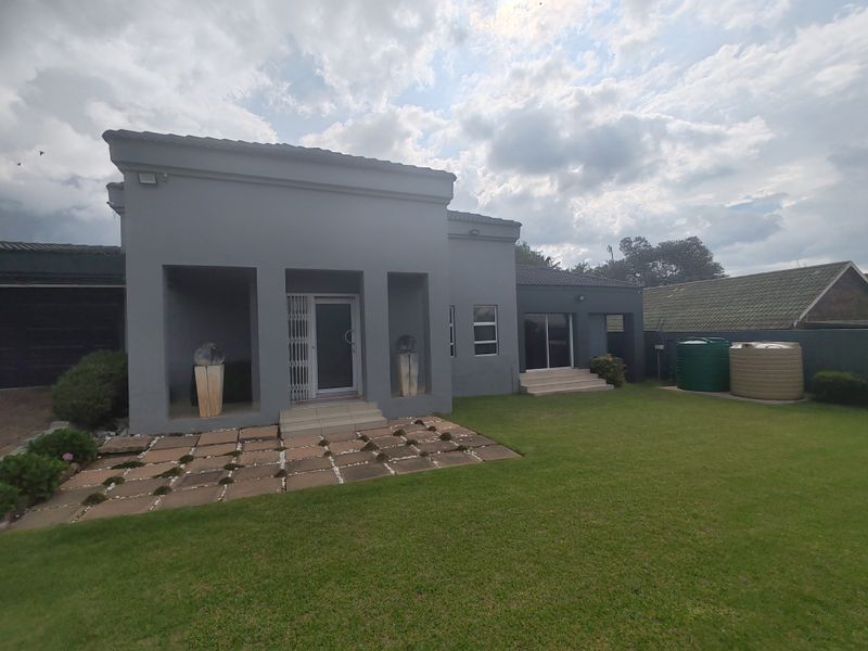 Rear view of the property featuring a grey facade, paved patio area, well-maintained lawn, and integrated water storage tanks.