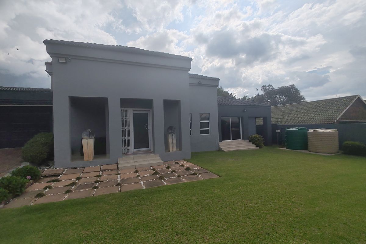 Rear view of the property featuring a grey facade, paved patio area, well-maintained lawn, and integrated water storage tanks.