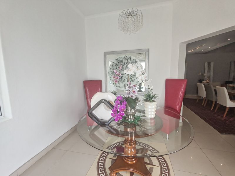 A bright dining area featuring polished floor tiles, a decorative coved ceiling, and an elegant crystal chandelier, creating a welcoming space for meals.