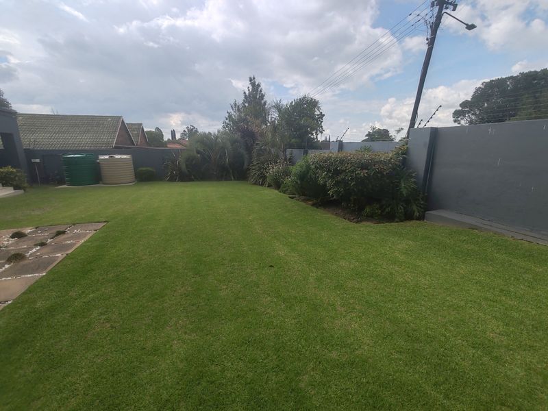A well-maintained private backyard featuring a lush green lawn, perimeter boundary walls with electric fencing, and convenient water storage tanks.