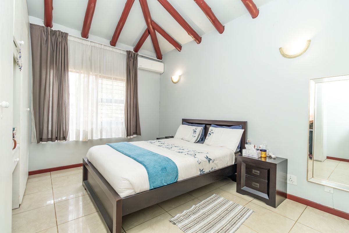 A bedroom featuring exposed timber ceiling beams, tiled flooring, and a wall-mounted air conditioning unit.